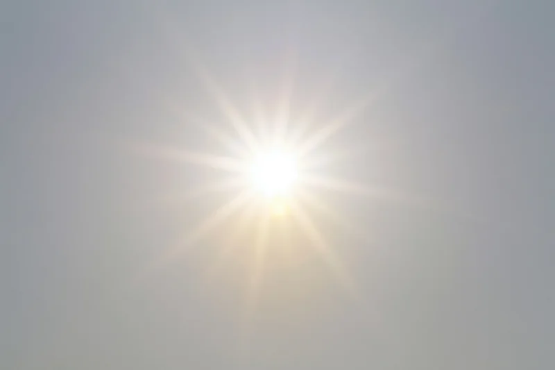 Bright sunburst lens flare radiating light rays from center against hazy sky