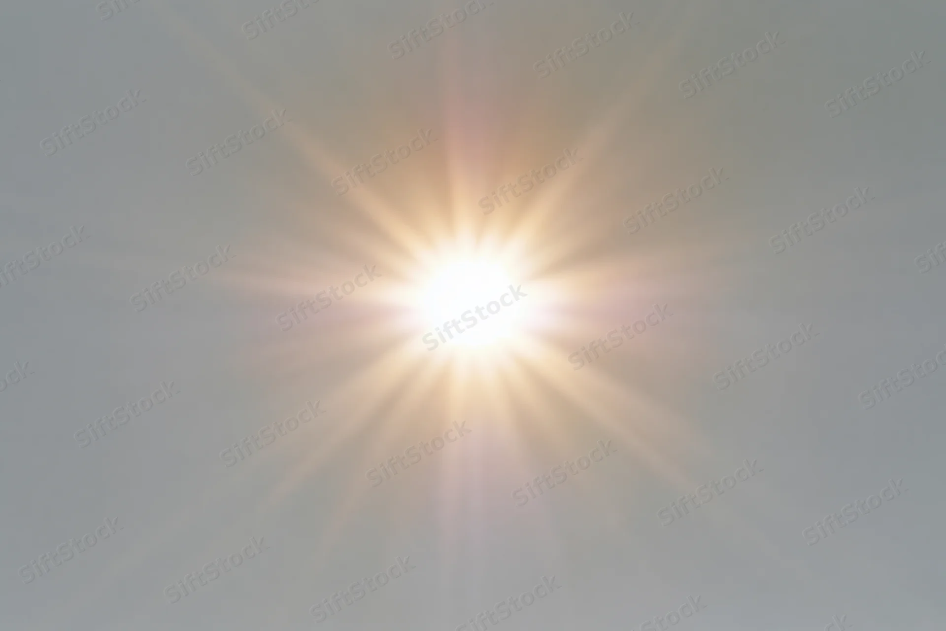 Bright sunburst lens flare radiating light rays from center of frame against hazy sky