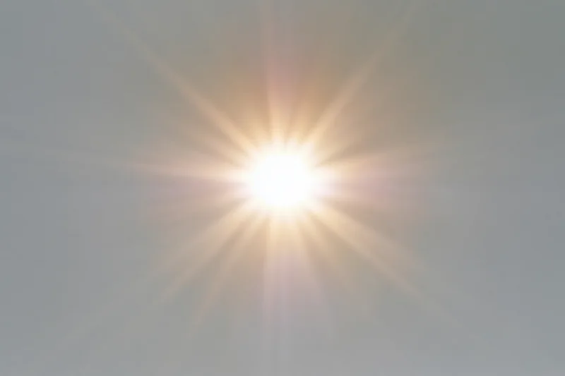 Bright sunburst lens flare radiating light rays from center of frame against hazy sky