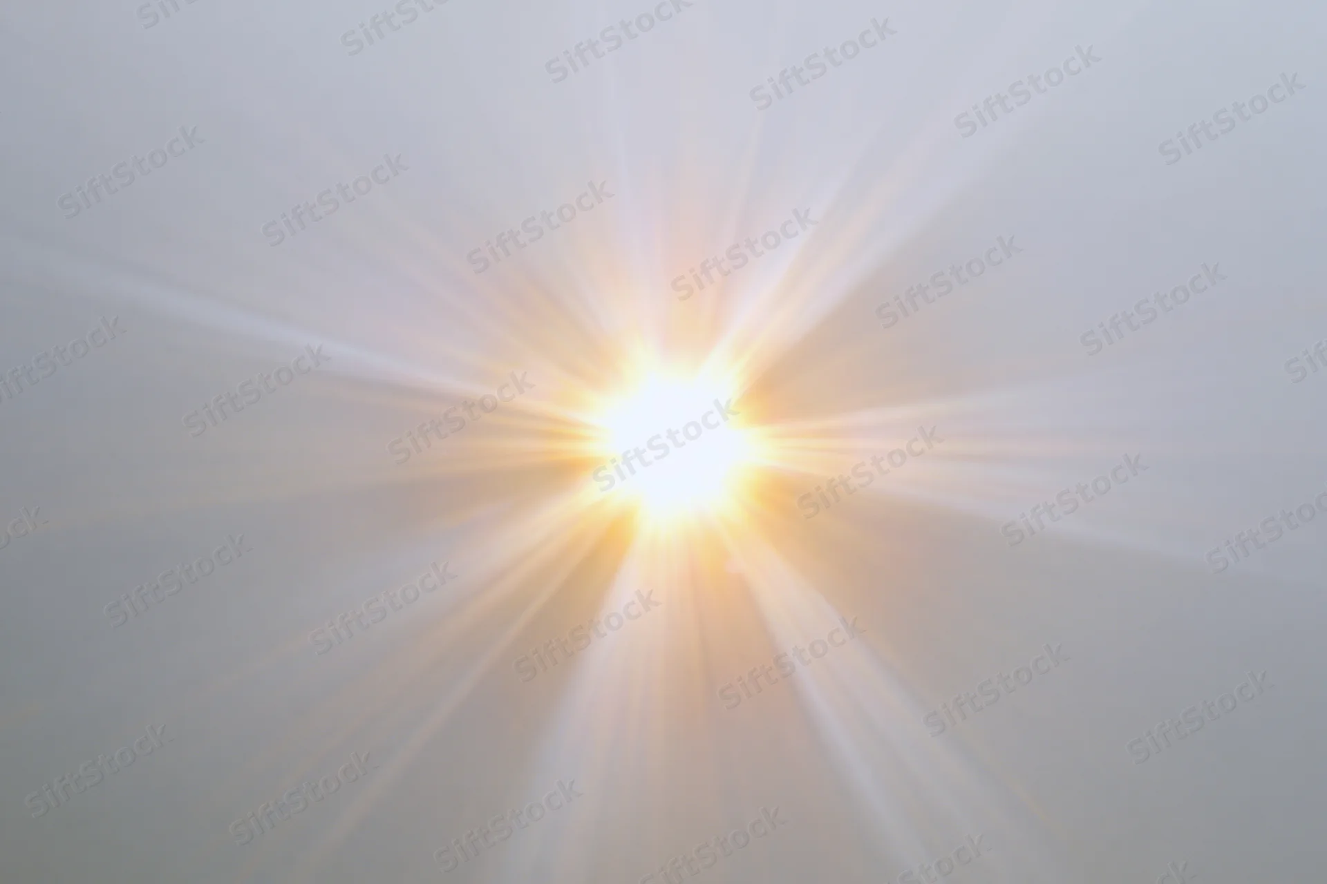 Bright sunburst lens flare radiating light rays from center against clear sky