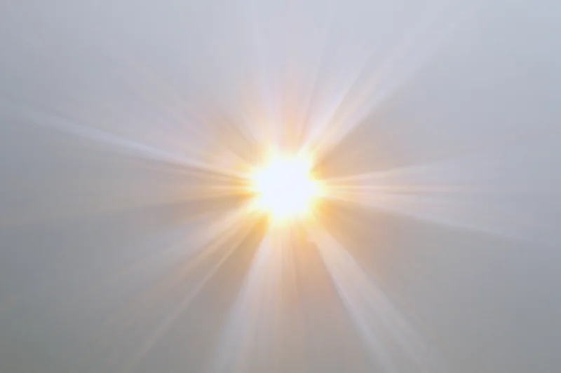 Bright sunburst lens flare radiating light rays from center against clear sky