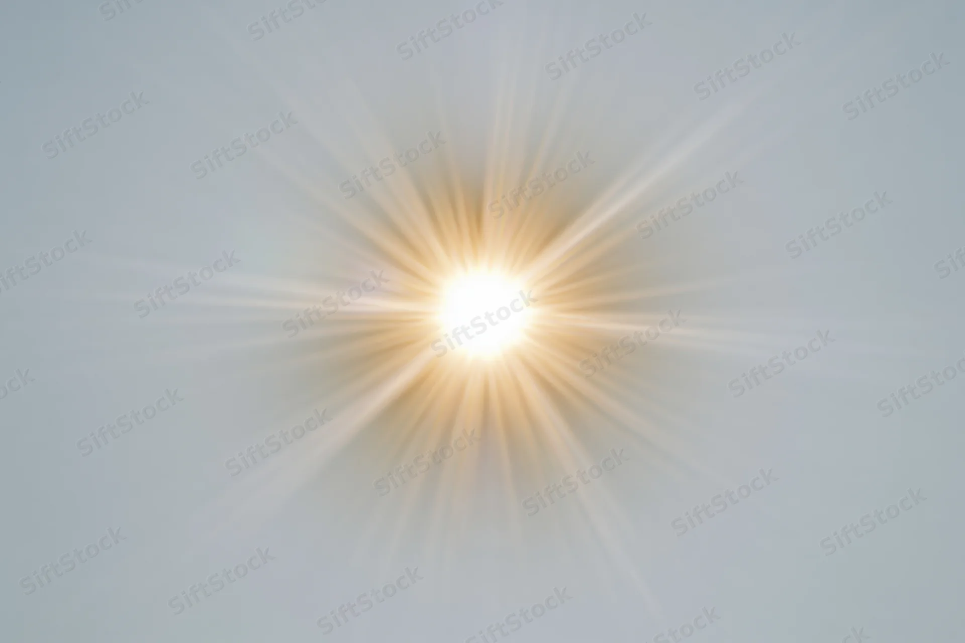 Bright sunburst lens flare radiating light rays from center against soft sky background