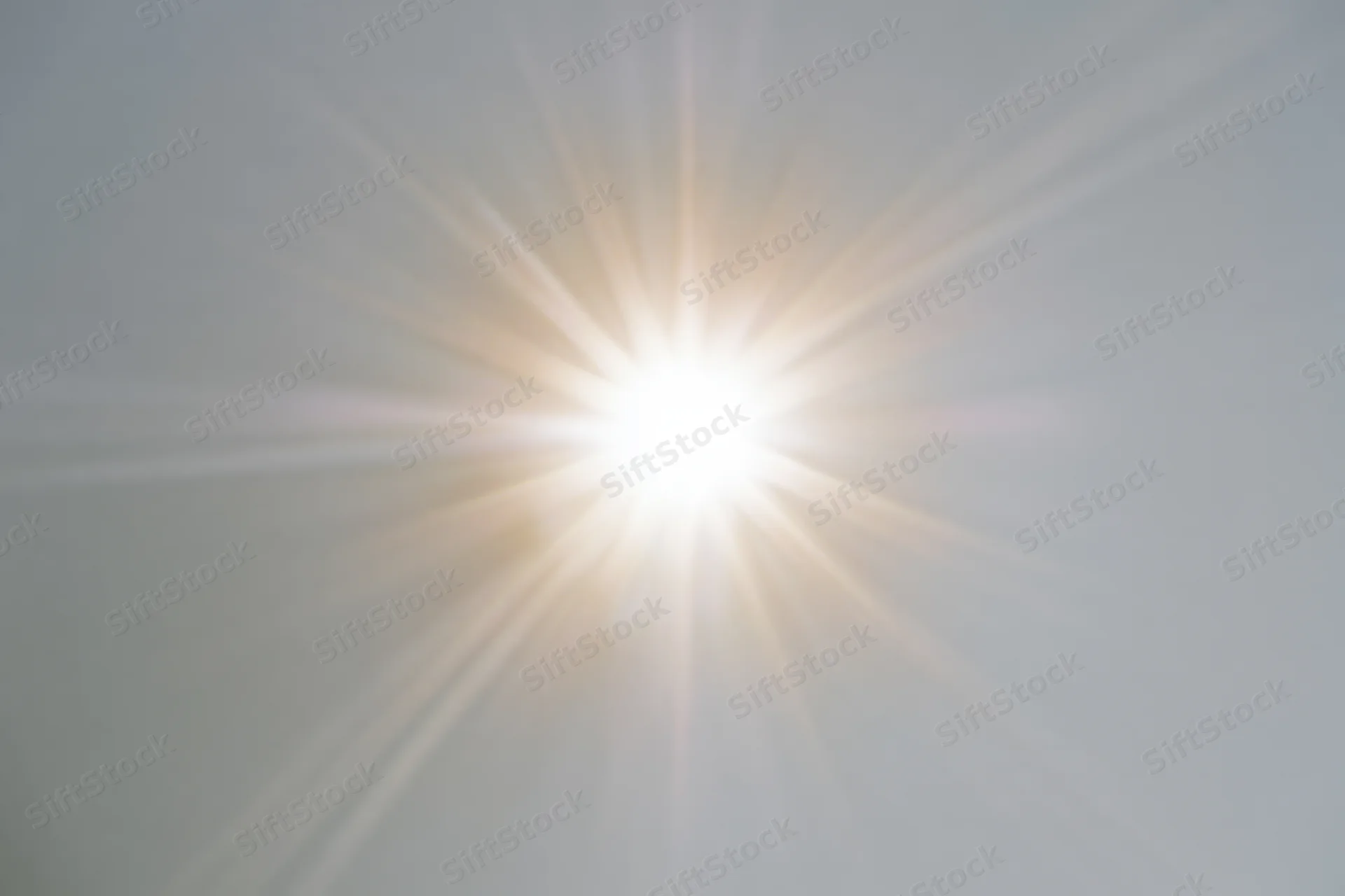 Bright sunburst lens flare radiating light rays from center frame against plain background