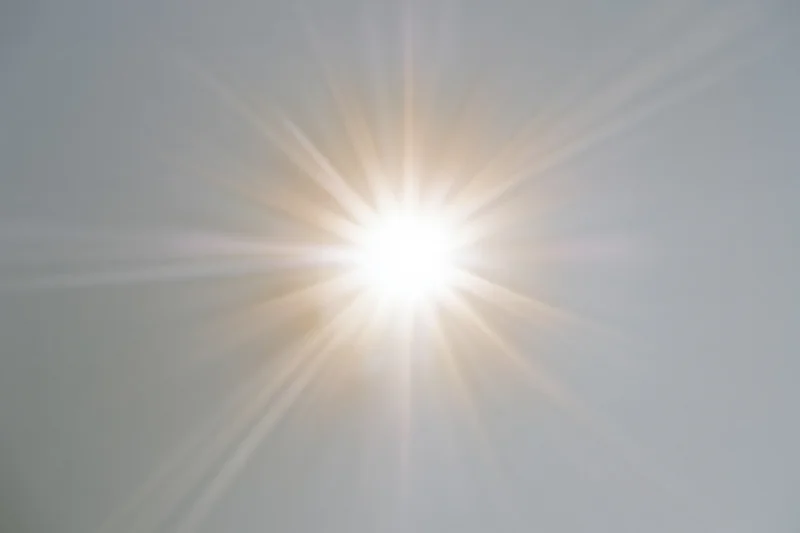 Bright sunburst lens flare radiating light rays from center frame against plain background