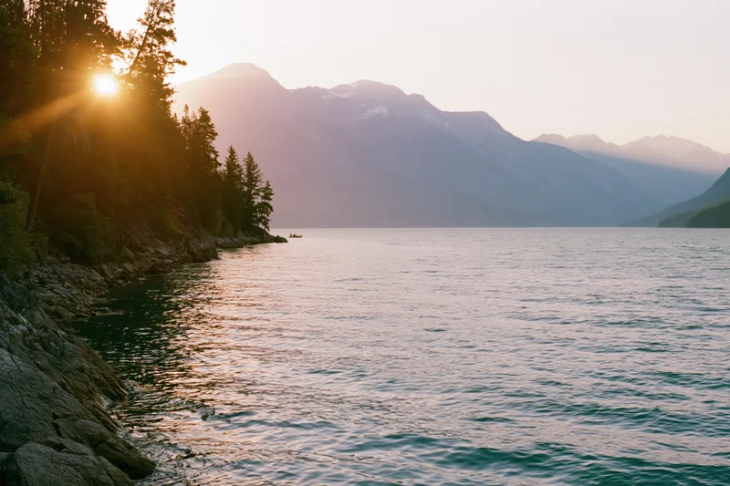 Calm alpine lake with rocky shoreline and dense evergreen forest at sunset