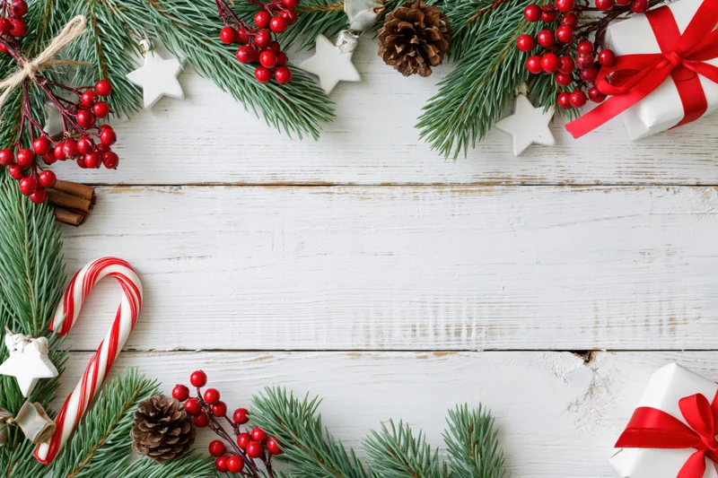 Christmas holiday flat lay with pine branches and red berries arranged on white wooden surface