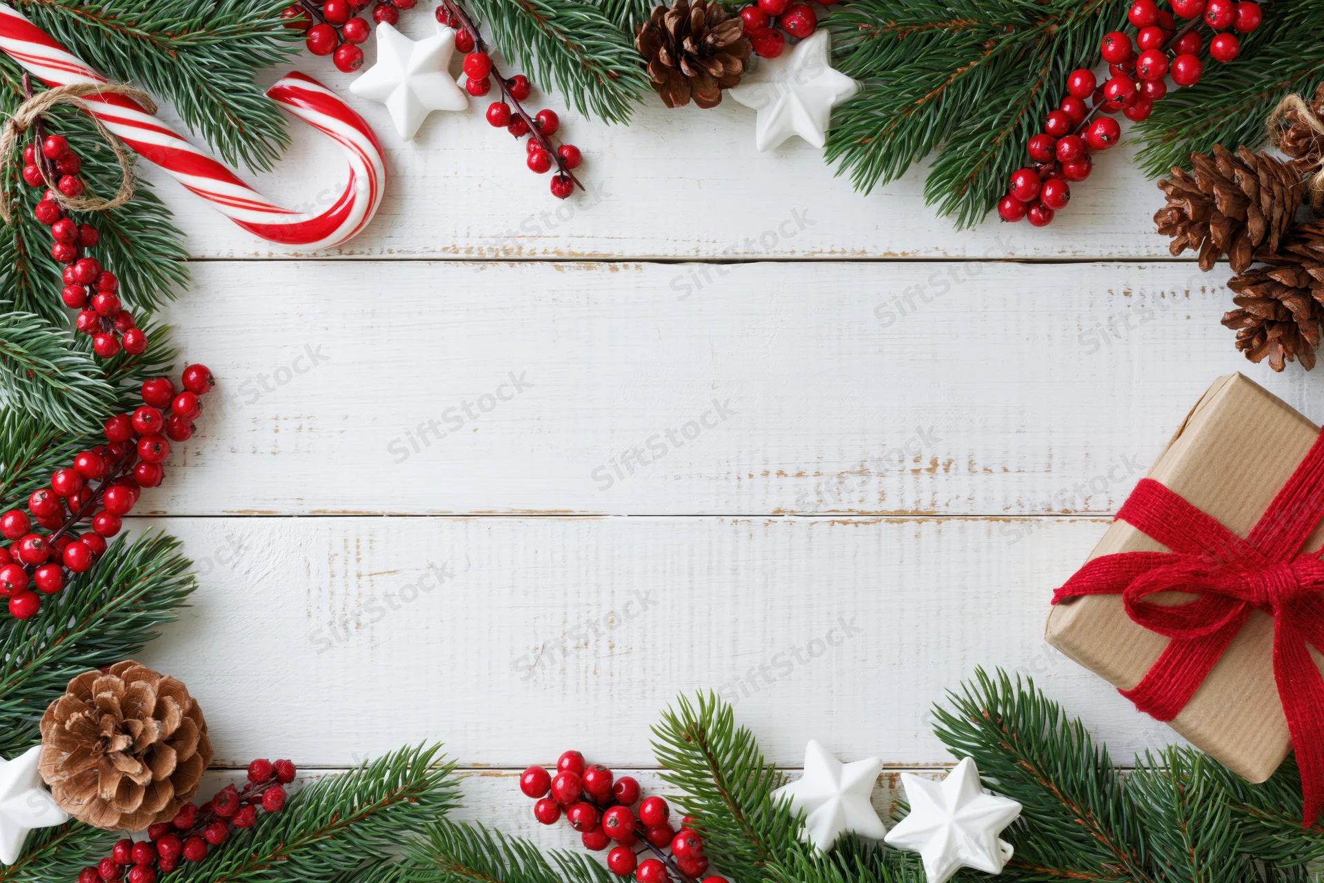 Christmas holiday flat lay with pine branches, red berries, candy canes, stars, pinecones, and a wrapped gift on white wooden surface