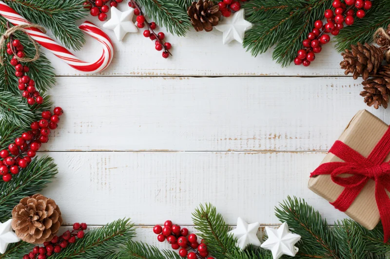 Christmas holiday flat lay with pine branches, red berries, candy canes, stars, pinecones, and a wrapped gift on white wooden surface