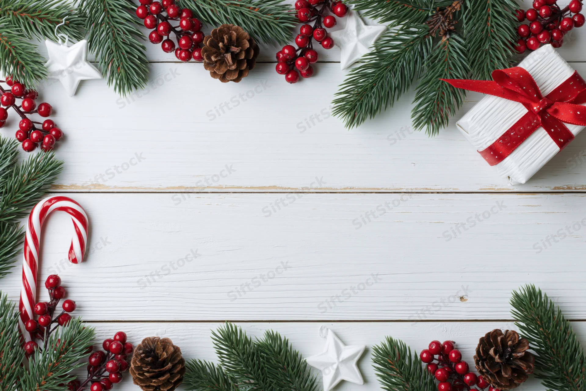 Christmas holiday flat lay with pine branches, red berries, candy cane, gift box, and pinecones arranged on white wooden surface