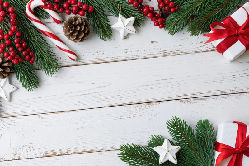 Christmas holiday flat lay with pine branches, red berries, candy canes, pinecones, stars, and gifts arranged on white wooden surface with copyspace