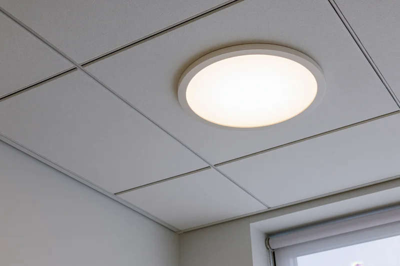 Circular recessed light fixture mounted in a white drop ceiling grid in an office interior