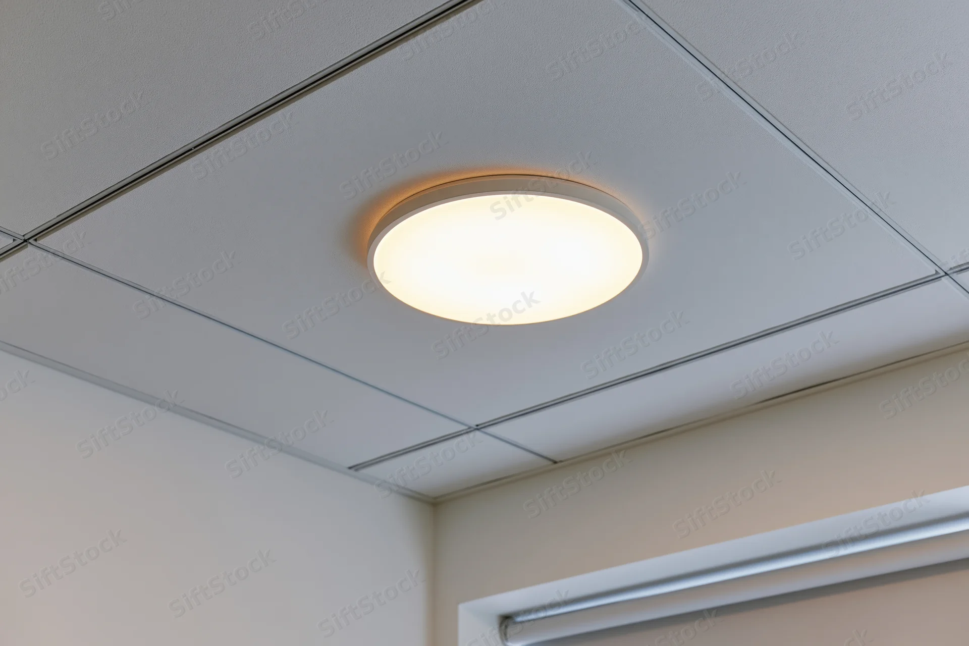 Recessed circular light fixture mounted in a white drop ceiling grid in an office interior