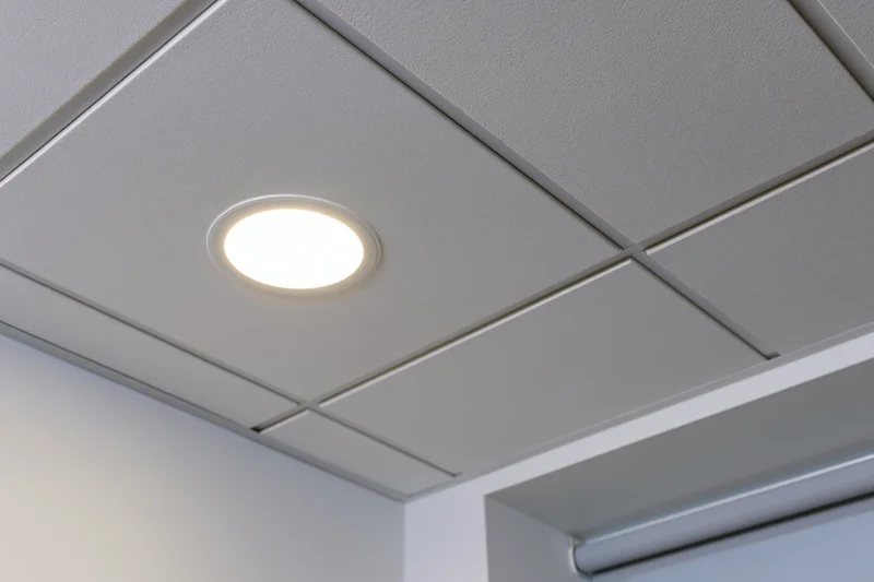 Close-up of a white drop ceiling tile with a recessed circular light in an office interior