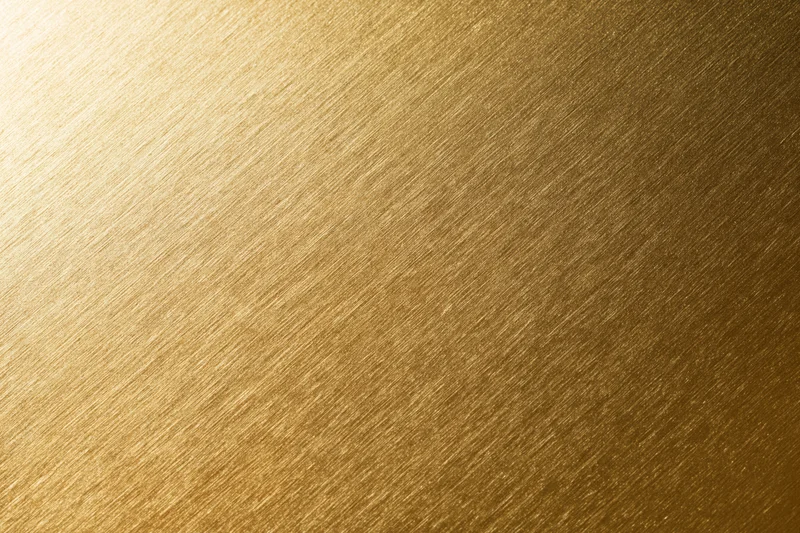 Close-up flat lay of a brushed gold metallic surface filling the frame with diagonal texture and warm gradient tone