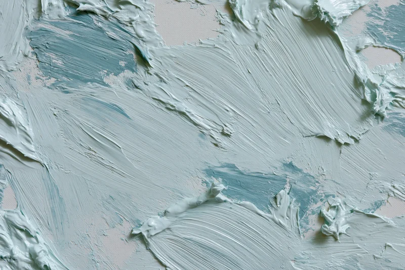 Close-up of white canvas with thick gestural blue and white paint strokes in flat lay arrangement