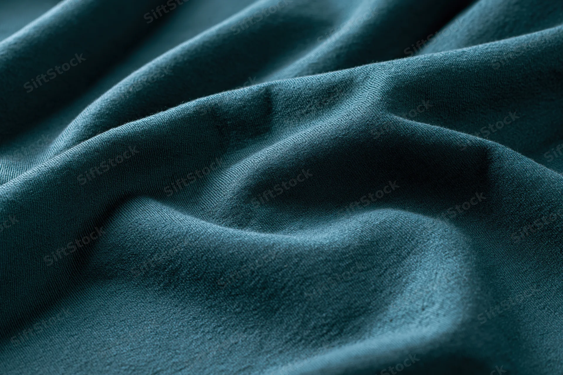 Close-up of deep teal-green fabric with soft folds and smooth texture filling the frame