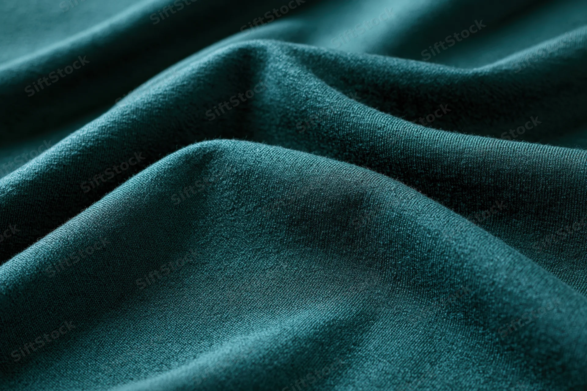 Close-up of deep teal-green fabric with soft folds and smooth texture filling the frame