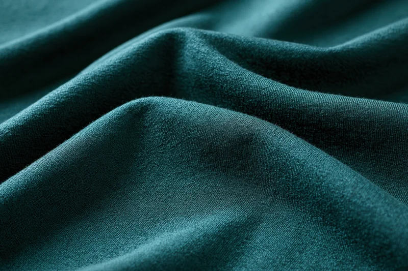 Close-up of deep teal-green fabric with soft folds and smooth texture filling the frame
