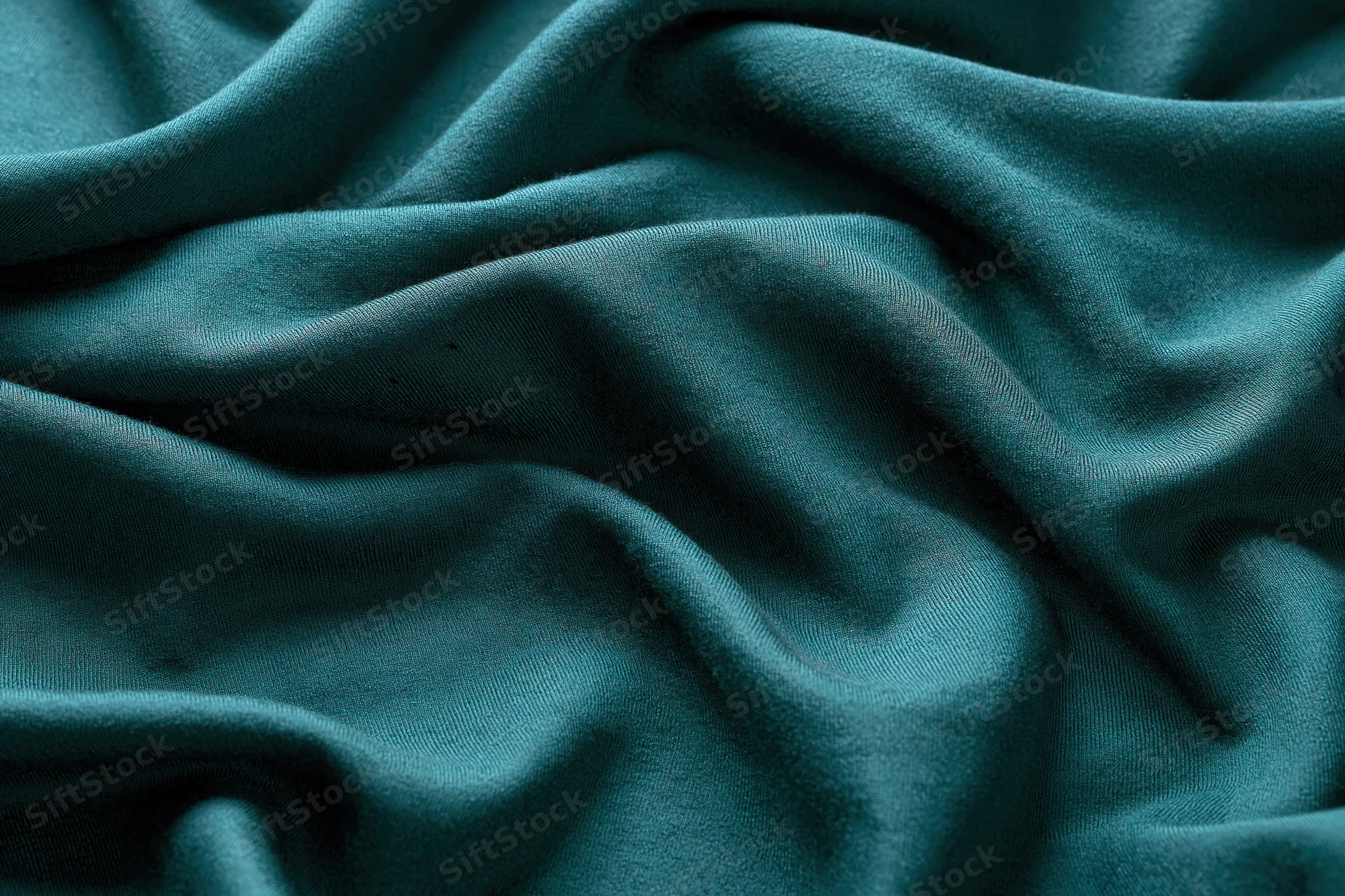 Close-up of deep teal-green fabric with natural folds and soft texture filling the frame