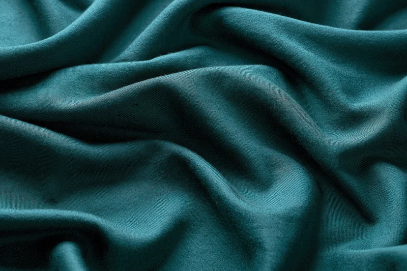 Close-up of deep teal-green fabric with natural folds and soft texture filling the frame