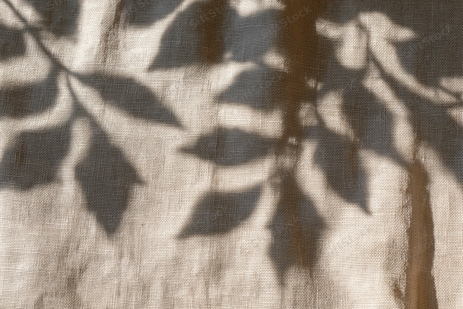 Natural linen fabric with leaf shadows cast across its surface in soft sunlight