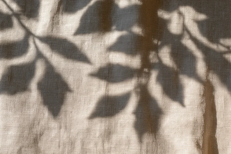 Natural linen fabric with leaf shadows cast across its surface in soft sunlight