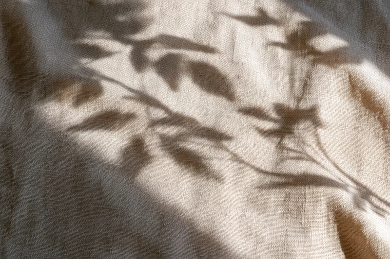 Natural linen fabric with leaf shadows cast across its surface in soft sunlight