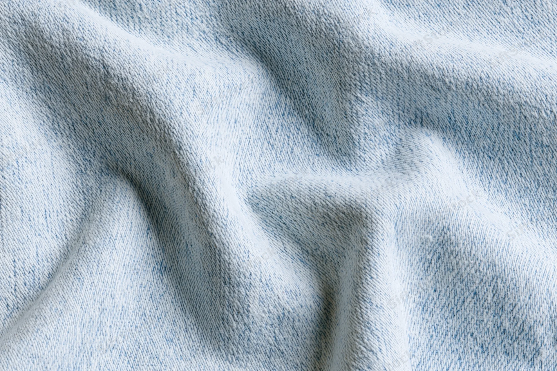 Close-up of light-wash denim fabric with visible weave and folds filling the frame