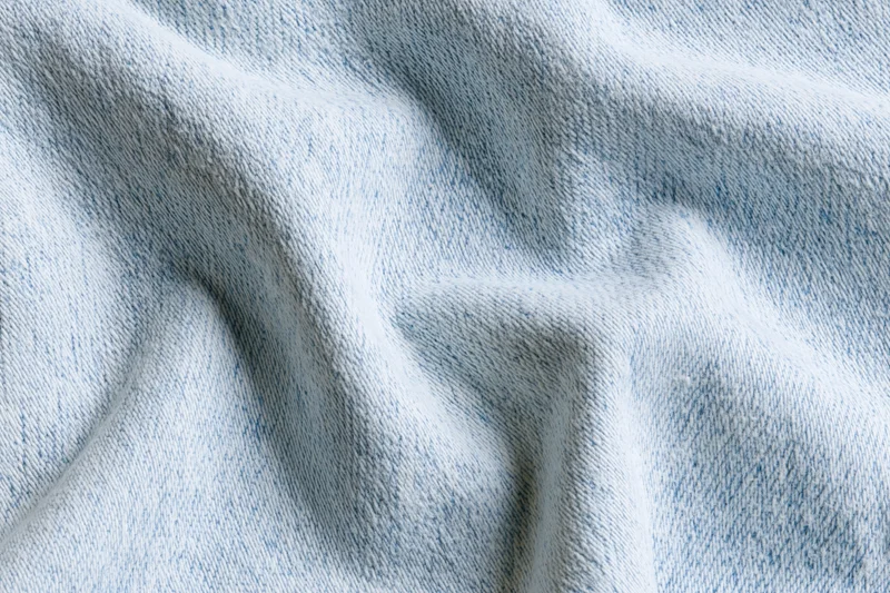 Close-up of light-wash denim fabric with visible weave and folds filling the frame