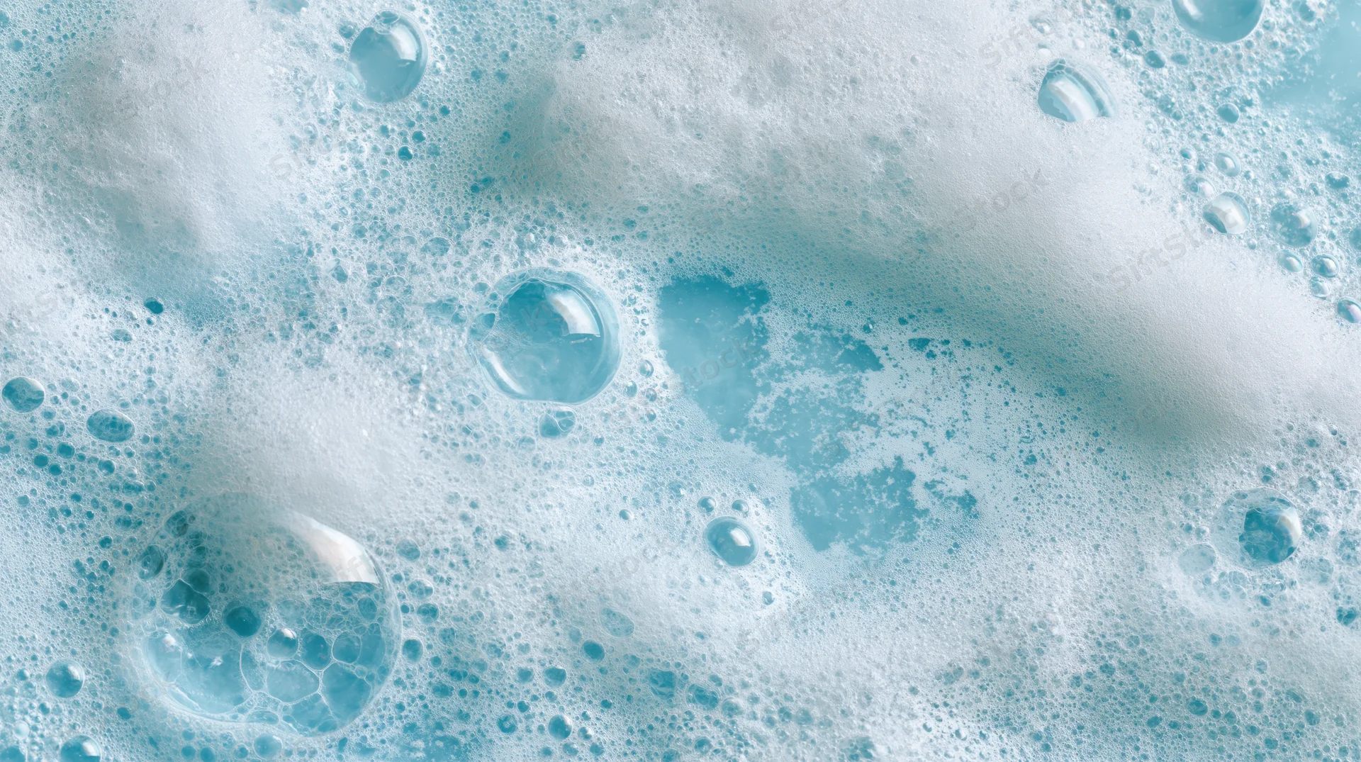 Close-up of white soapy foam and bubbles floating on a blue liquid surface