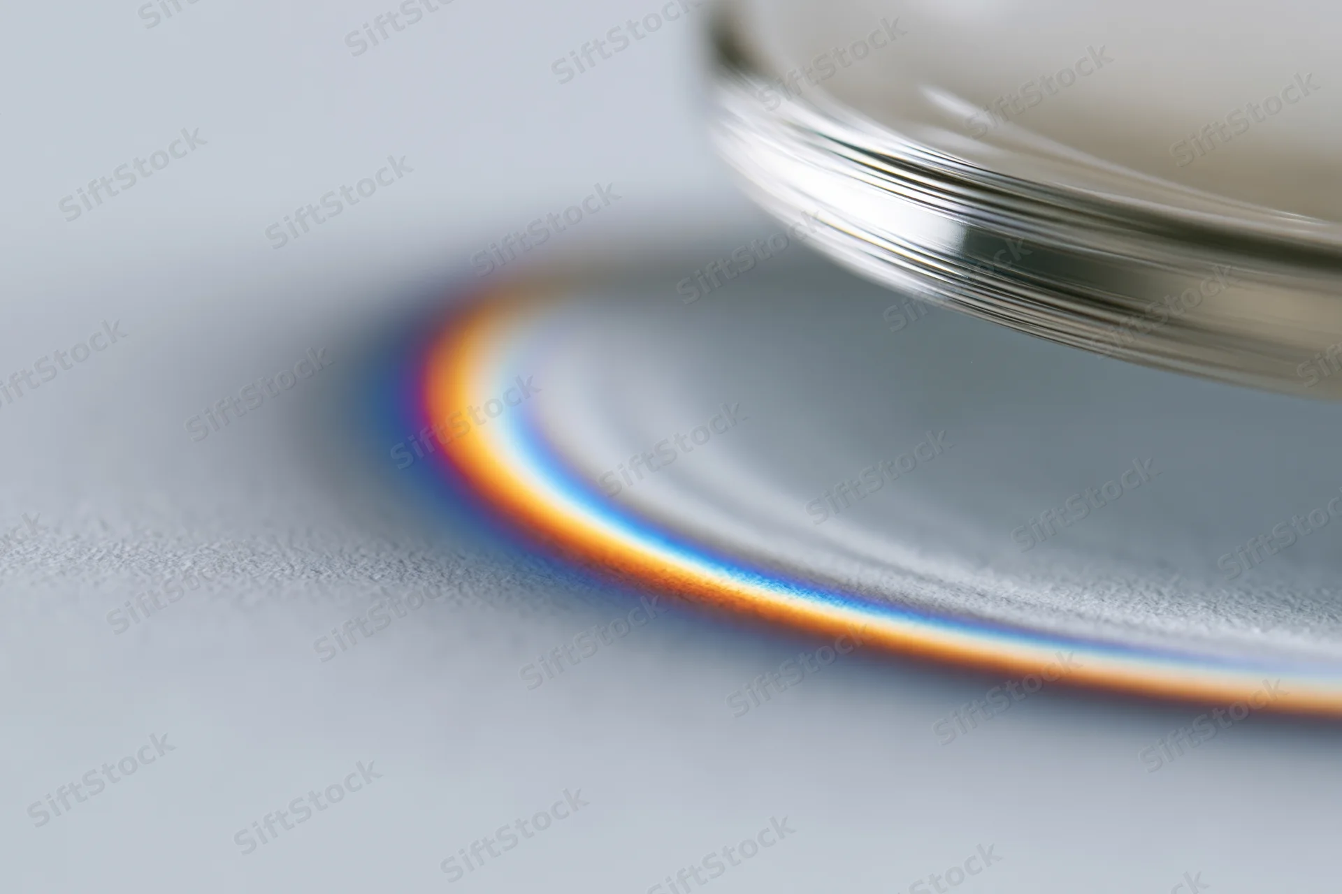 Close-up of a glass prism edge casting a rainbow spectrum on a gray surface