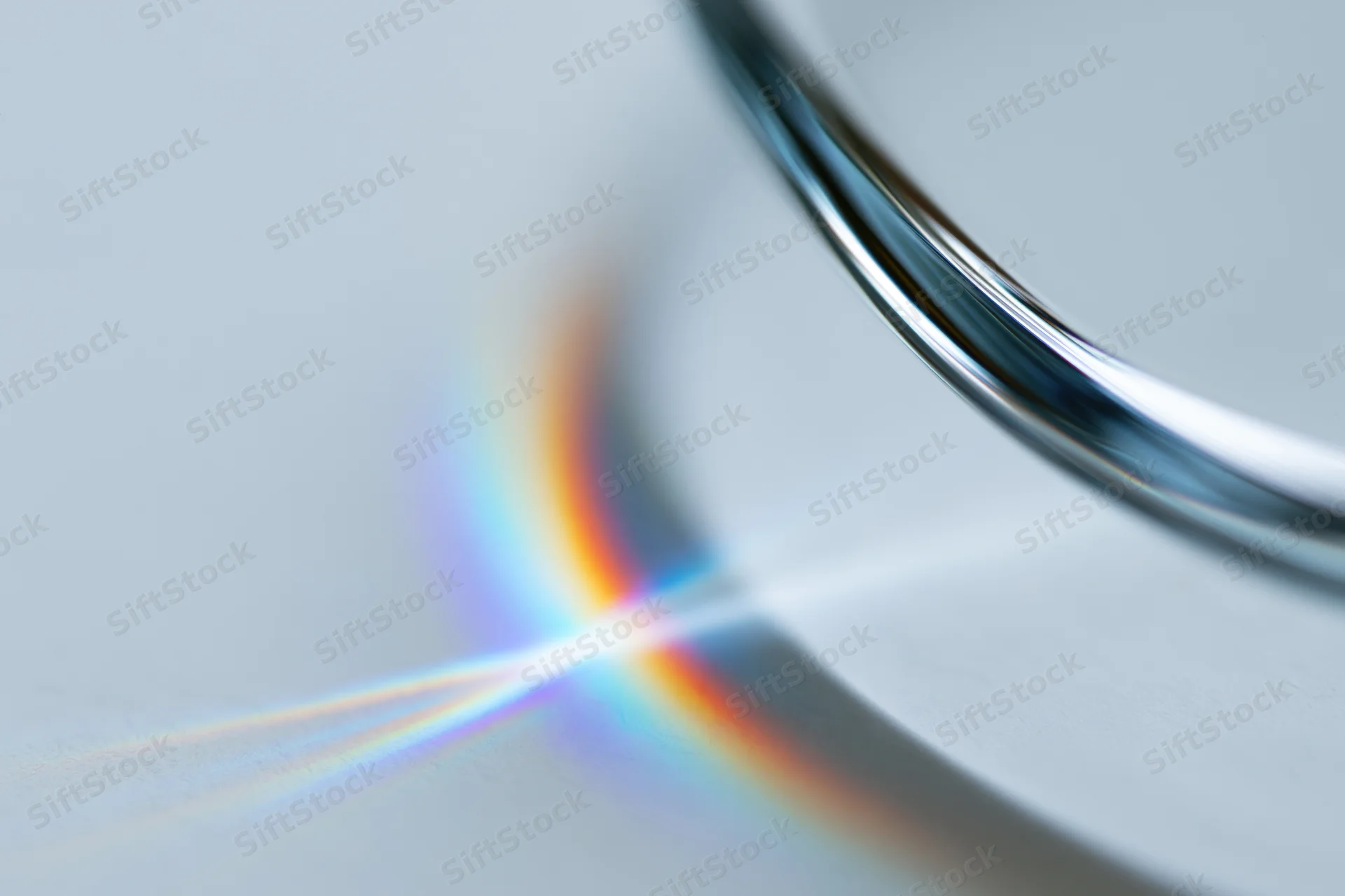 Close-up of a glass prism edge refracting light into a rainbow spectrum on a white surface