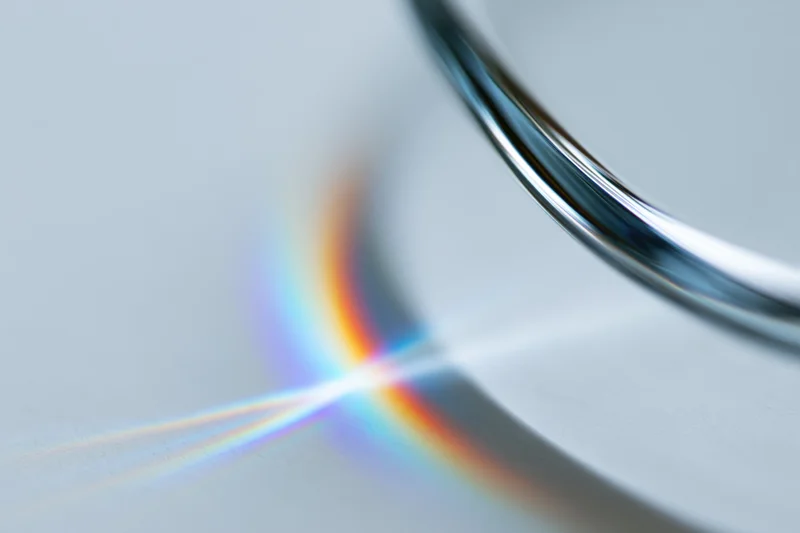 Close-up of a glass prism edge refracting light into a rainbow spectrum on a white surface