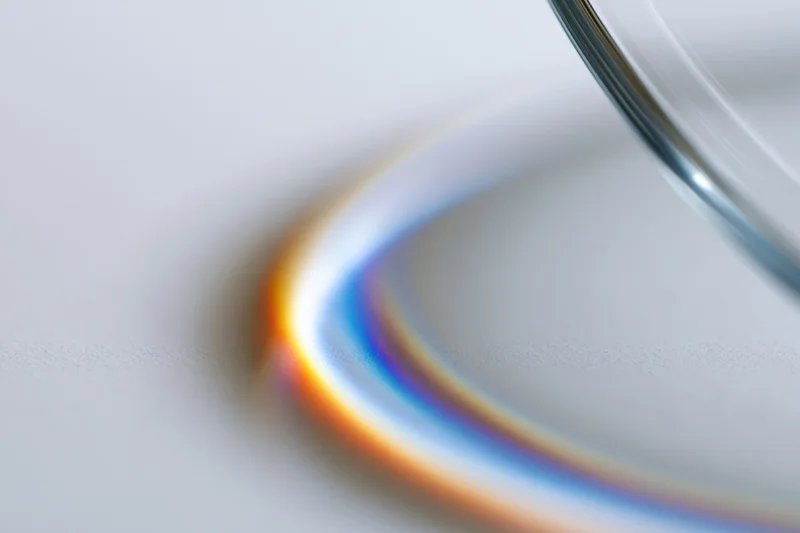 Close-up of a glass prism edge casting a rainbow spectrum on a white surface through light refraction