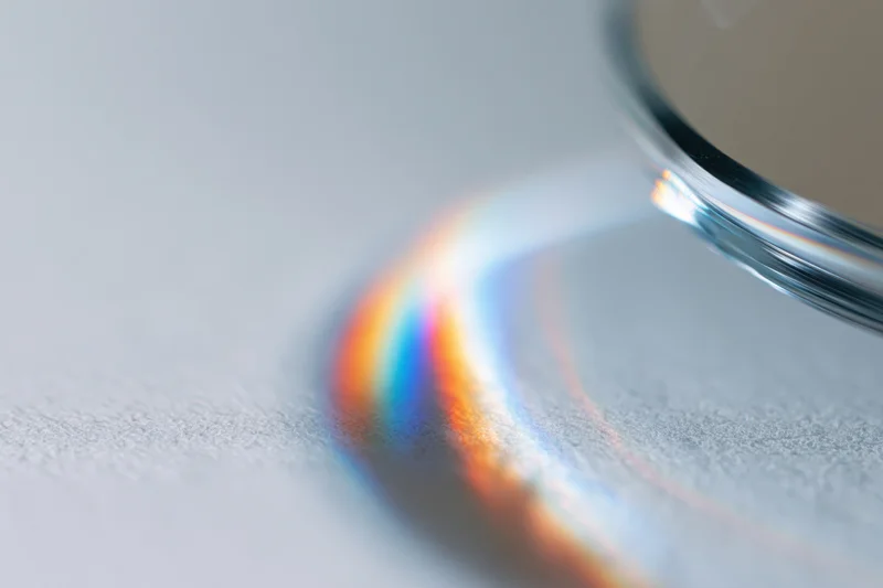 Glass prism edge casting a rainbow spectrum on a white textured surface