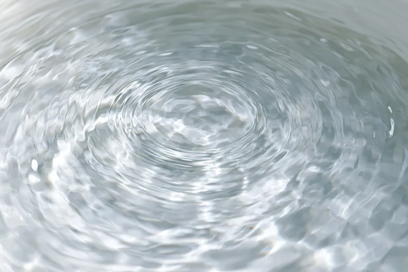 Calm clear water surface with gentle ripples spreading outward from a central point