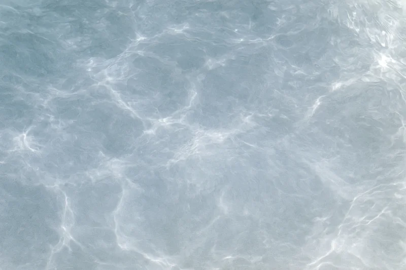 Calm clear water surface with gentle ripples and light reflections overhead
