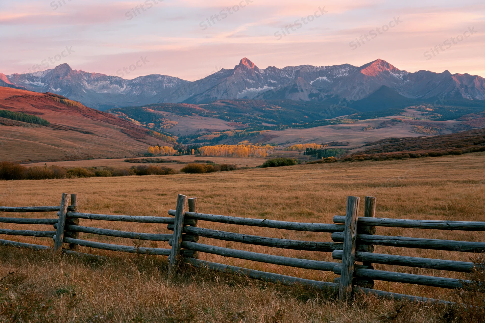 Wide valley with wooden fence and distant Rocky Mountains at sunset in autumn Colorado landscape