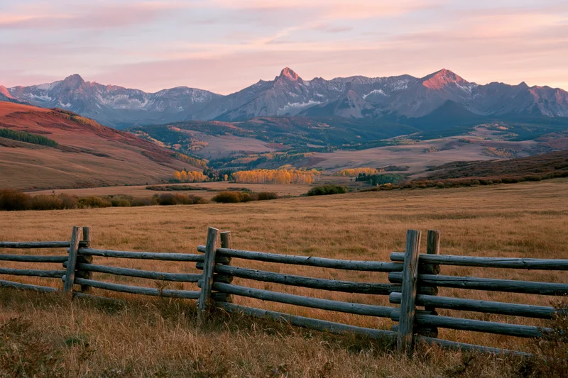 Wide valley with wooden fence and distant Rocky Mountains at sunset in autumn Colorado landscape