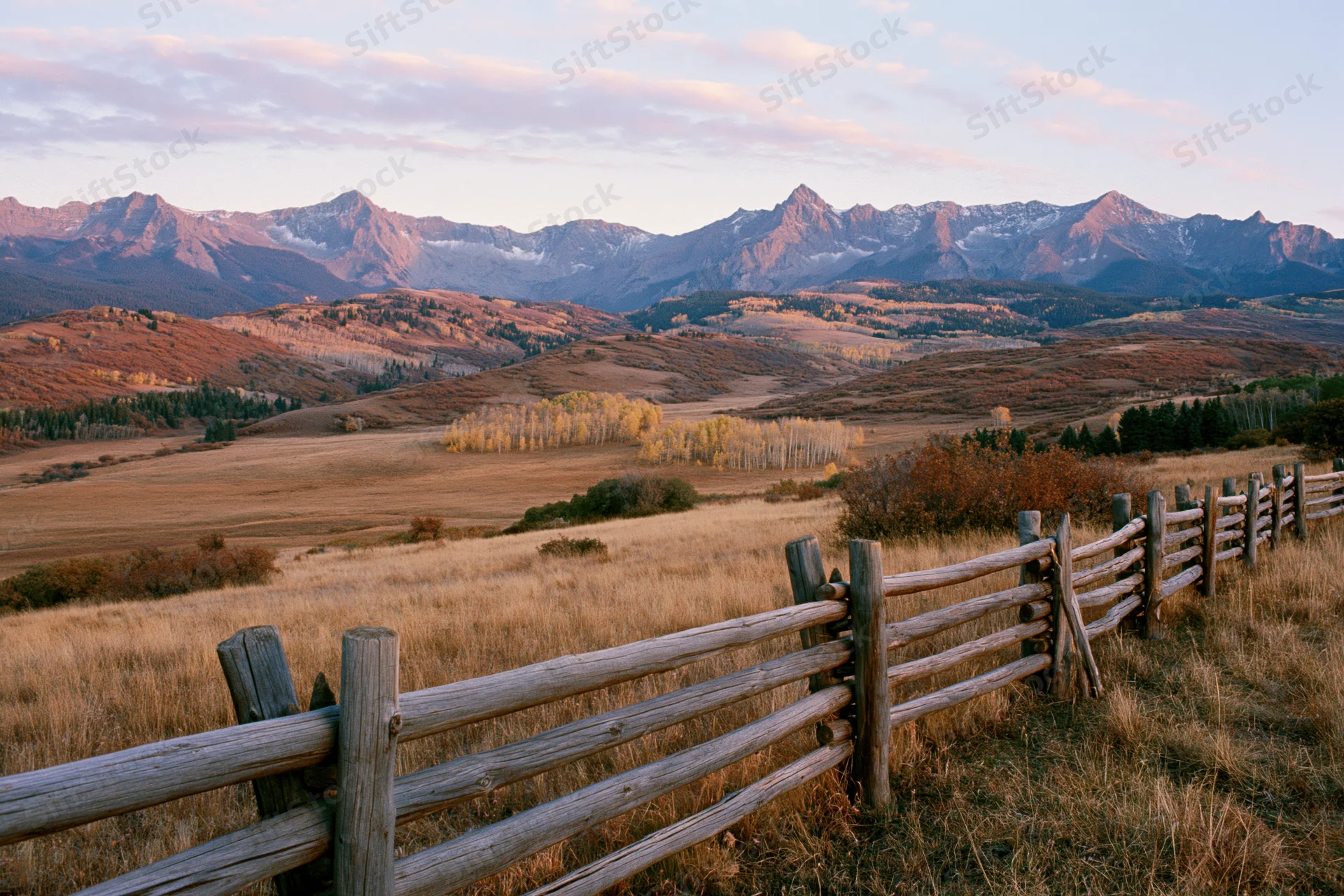Wooden fence along a grassy valley with mountains in the distance at sunset in autumn