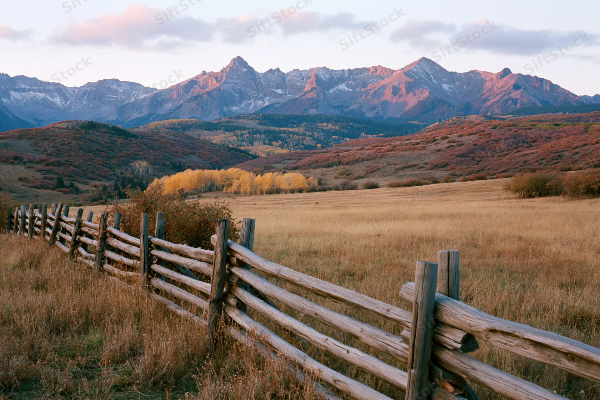 Wooden fence along a grassy valley at sunset with mountains in the background during autumn