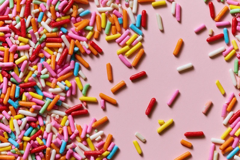 Colorful candy sprinkles scattered across a flat pink surface