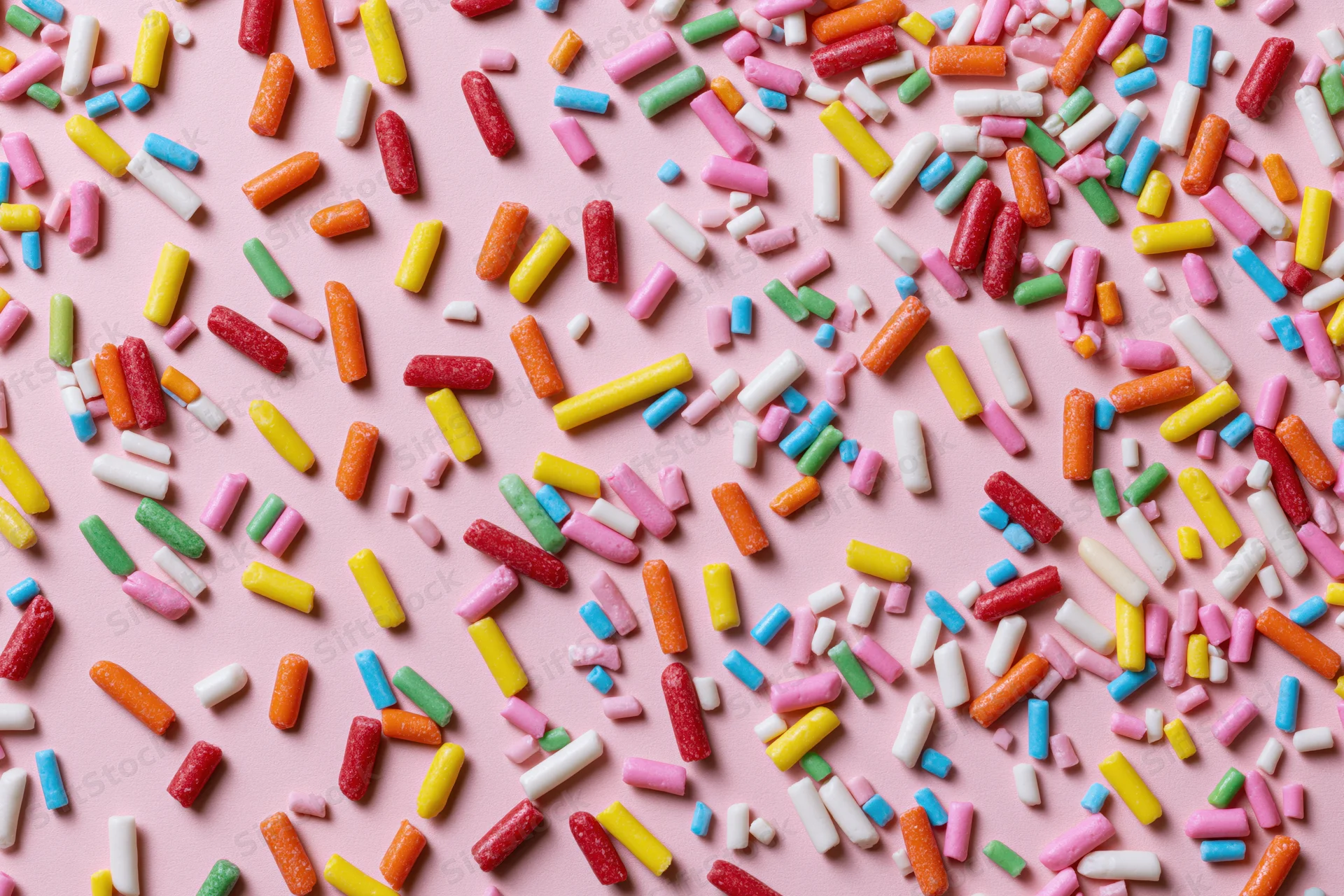 Colorful candy sprinkles scattered randomly across a flat pink surface