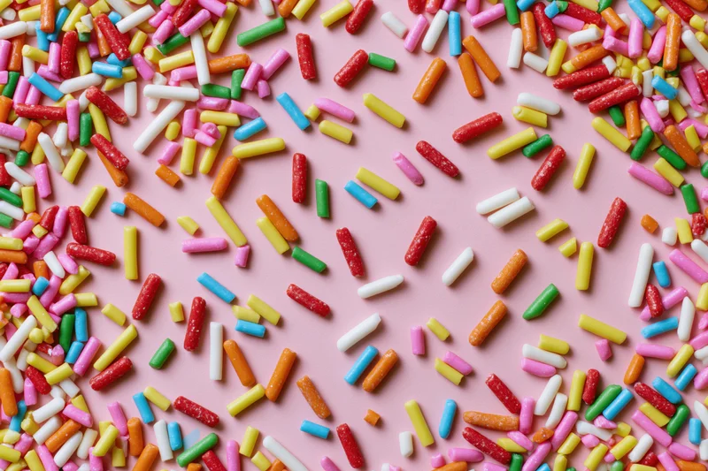 Colorful candy sprinkles scattered randomly across a flat pink surface
