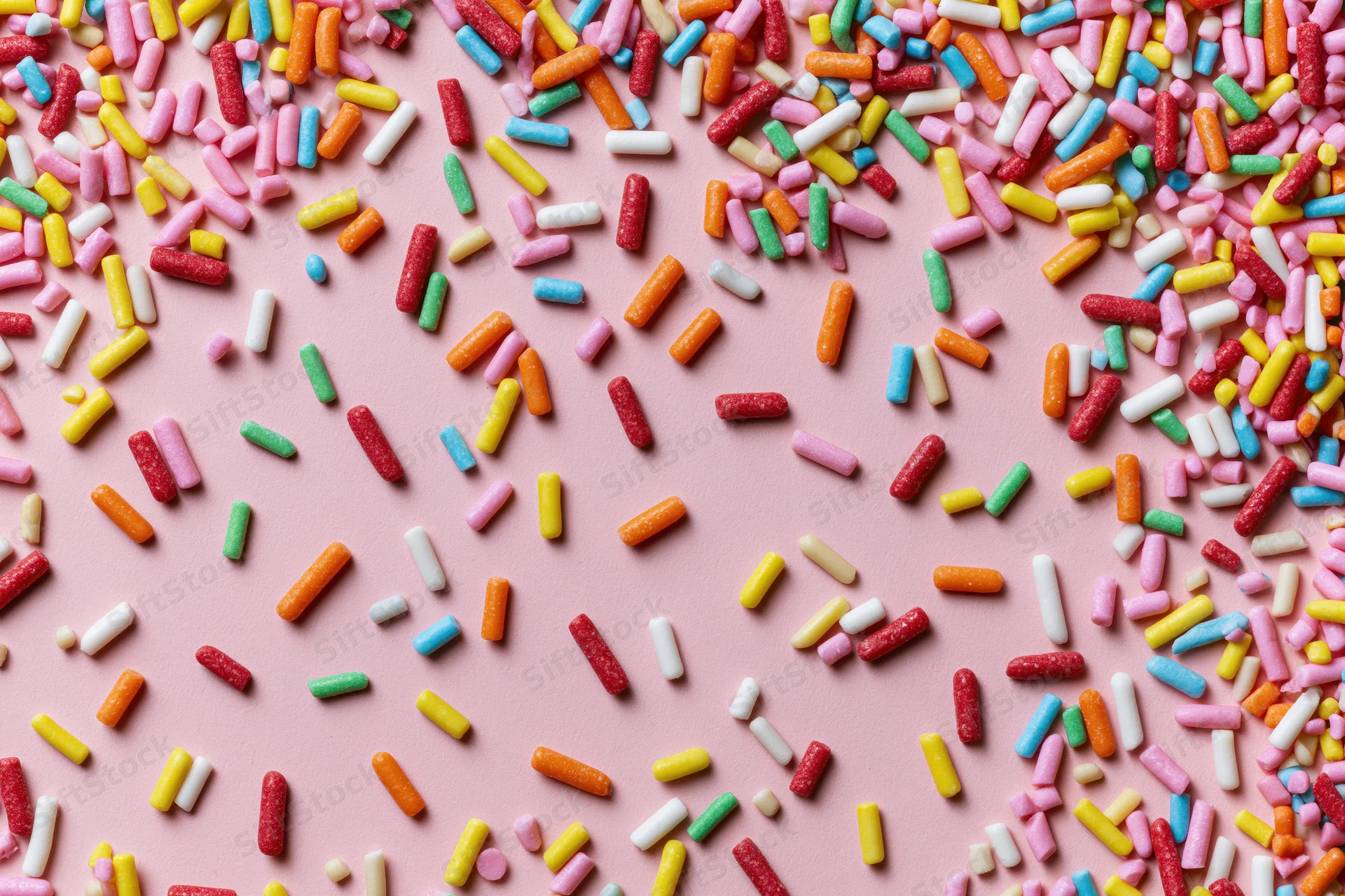Colorful candy sprinkles scattered randomly across a flat pink surface