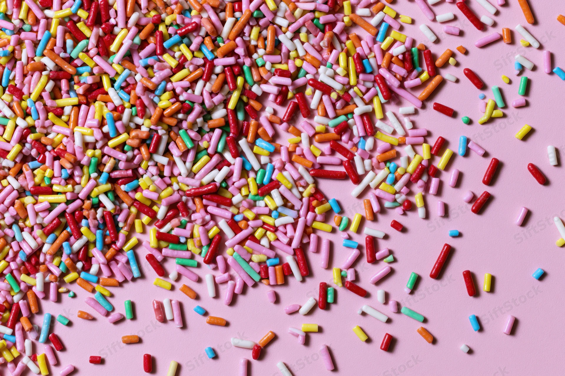 Colorful candy sprinkles scattered randomly across a flat pink surface