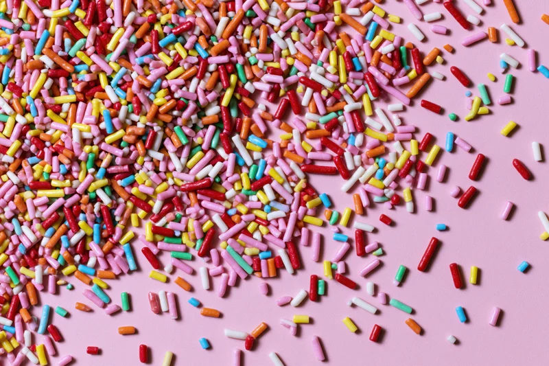 Colorful candy sprinkles scattered randomly across a flat pink surface