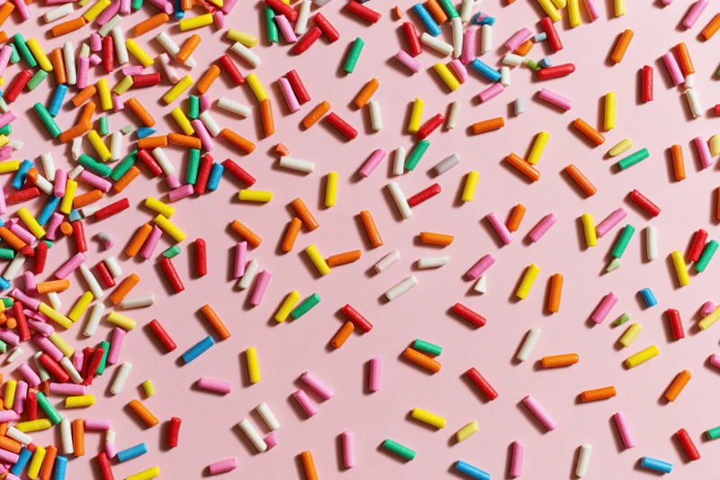 Colorful candy sprinkles scattered randomly across a flat pink surface
