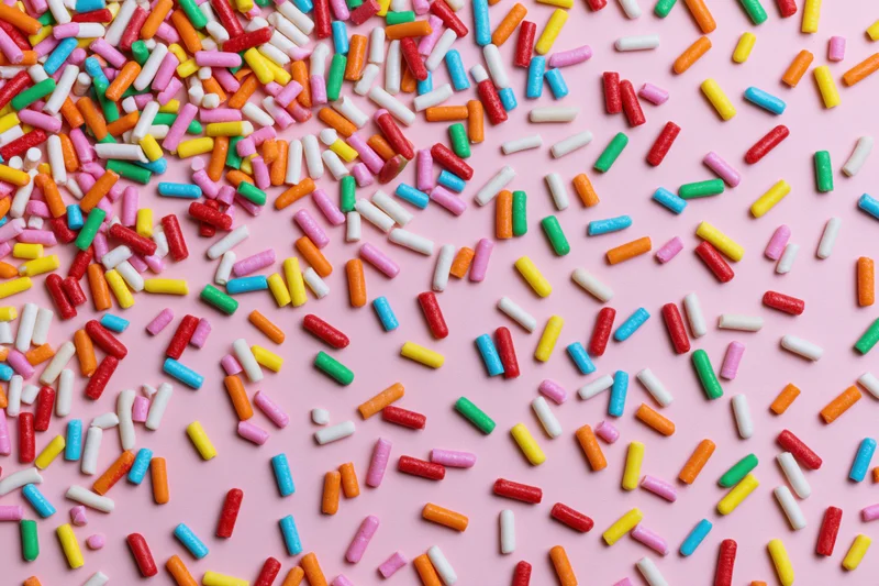 Colorful candy sprinkles scattered randomly across a flat pink surface