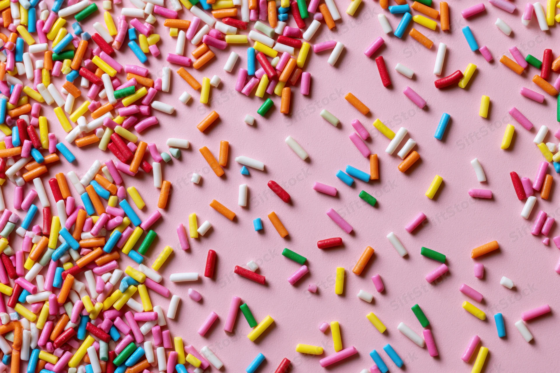 Colorful candy sprinkles scattered randomly across a flat pink surface